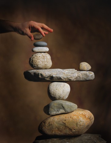 abstract photograph of hands trying to carefully balance a pile of rocks